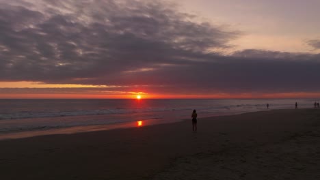 Slow-aerial-dolly-past-a-young-woman-taking-photos-of-the-vibrant-sunset-at-Iquique