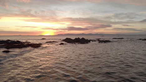 Lufttiefflug-Vorwärts-über-Meerwasser-Mit-Einem-Wunderschönen-Orangefarbenen-Sonnenaufgang-Am-Horizont