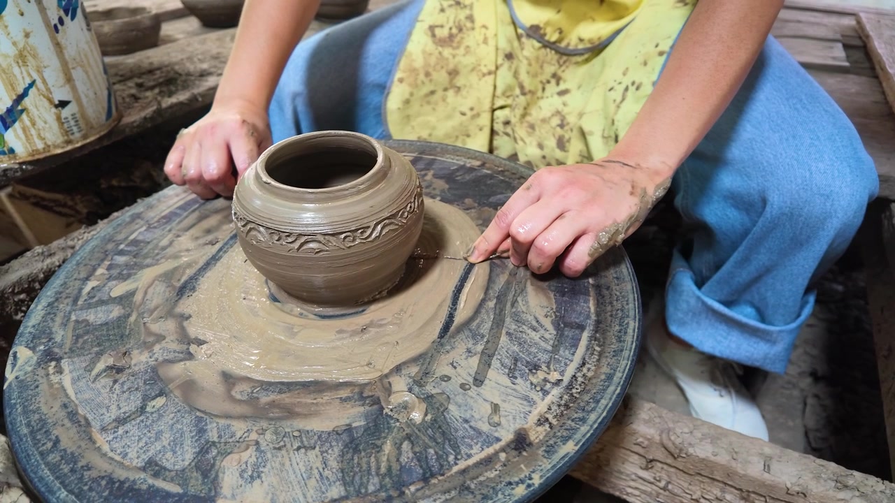 Primo piano di un vasaio che usa un filo per tagliare un vaso di ceramica finito dal tornio a Nonthaburi