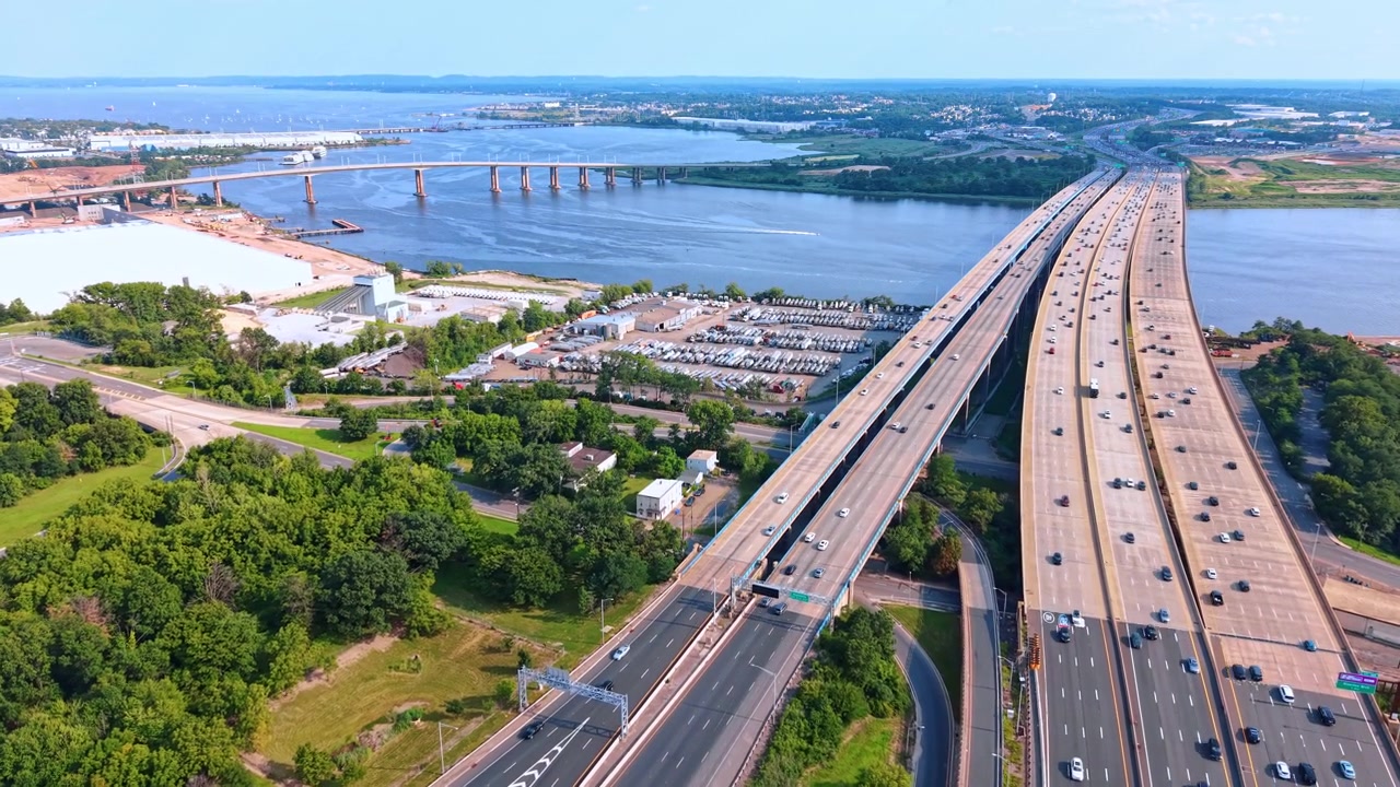 Ampio ponte autostradale che attraversa il fiume tra alberi verdi, New Jersey, USA. Scatto aereo ad alta quota di lunghe strade asfaltate, acqua blu e foresta lussureggiante.