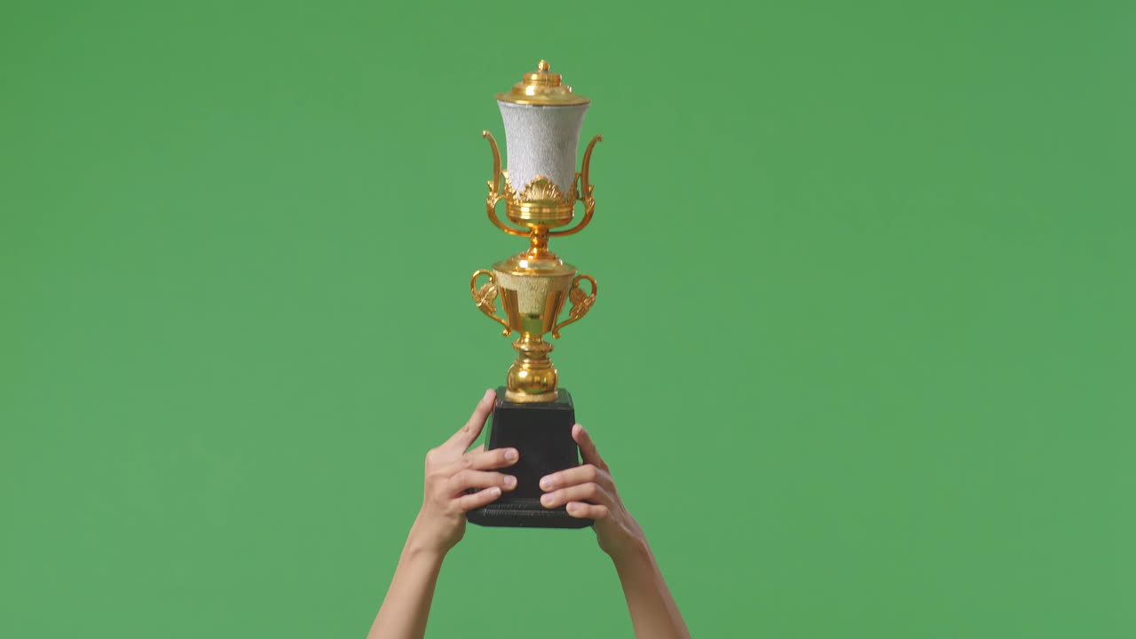 한 여성의 손이 트로피를 들고 있다. 녹색 화면 배경