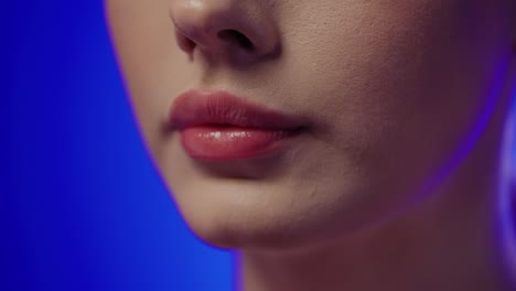 Extreme-Nahaufnahme-Einer-Jungen-Frau-Mit-Schönen-Roten-Lippen,-Die-Vor-Blauem-Hintergrund-In-Zeitlupe-Eine-Kapsel-Für-Ihre-Gesundheit-Mit-Gesunden-Zutaten-Einnimmt