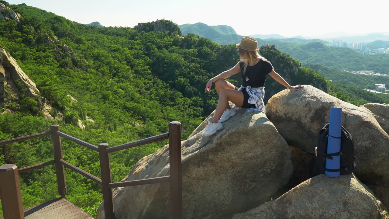 niña sentada en las rocas con bosque verde y horizonte de la ciudad en el fondo de la montaña gwanaksan en seúl, corea del sur