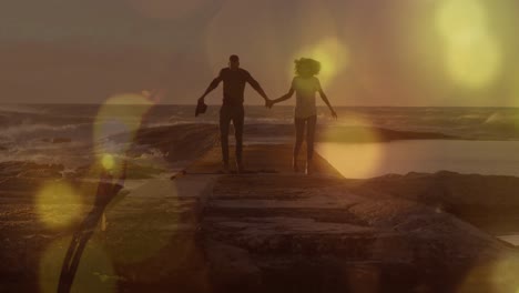 manchas amarillas de luz sobre una pareja afroamericana cogida de la mano caminando sobre las rocas cerca del mar