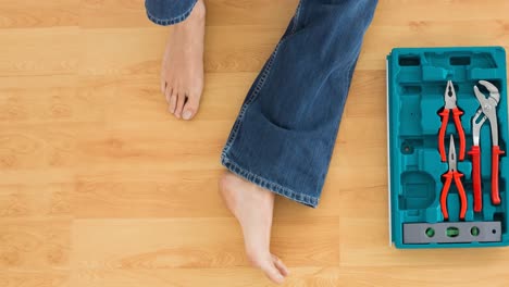 animación de pies descalzos de mujer en vaqueros sentada en el suelo de madera con caja de herramientas abierta