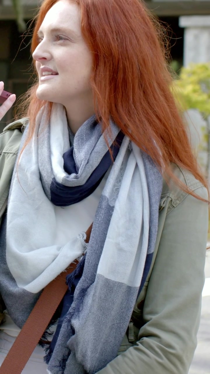 Vídeo vertical: Mulher com lenço levantando o celular, fazendo uma ligação em um smartphone rosa na praça, com espaço para texto.