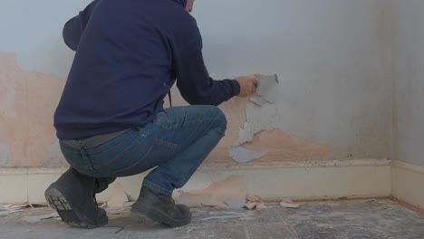 adult working to scrap away blistered paint from interior wall