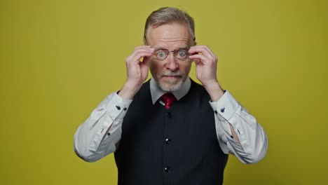 portrait of a serious elderly man with glasses. senior businessman putting on glasses and becomes happy on yellow background. positive emotions.