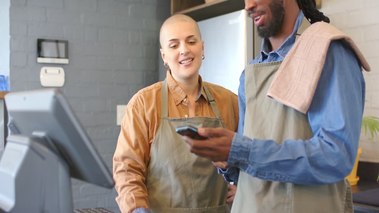 Diverse baristas at cafe counter initiating payment by smartwatch tapping reader and typing PIN