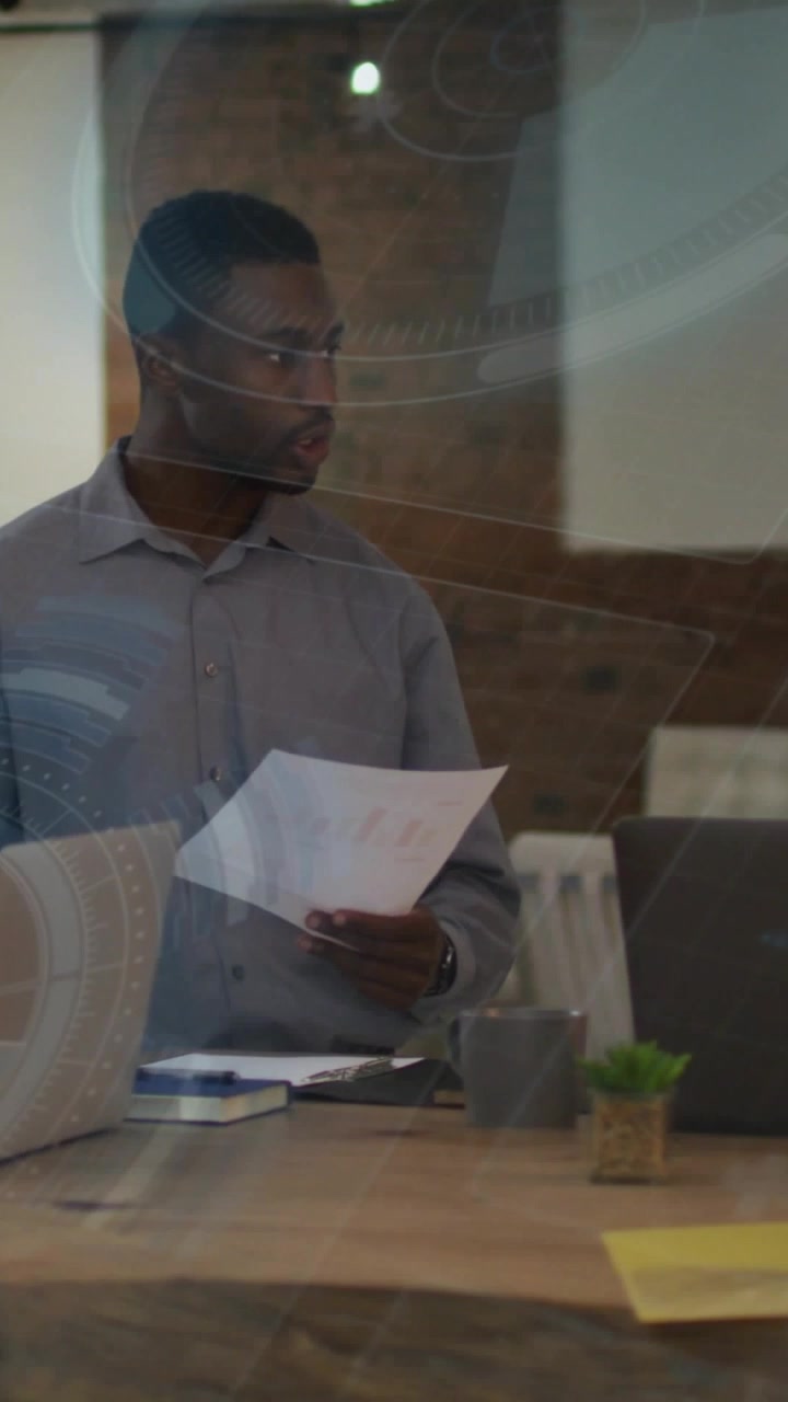 Vertical video: Business man picking report, reading, checking laptop for call while lights moving