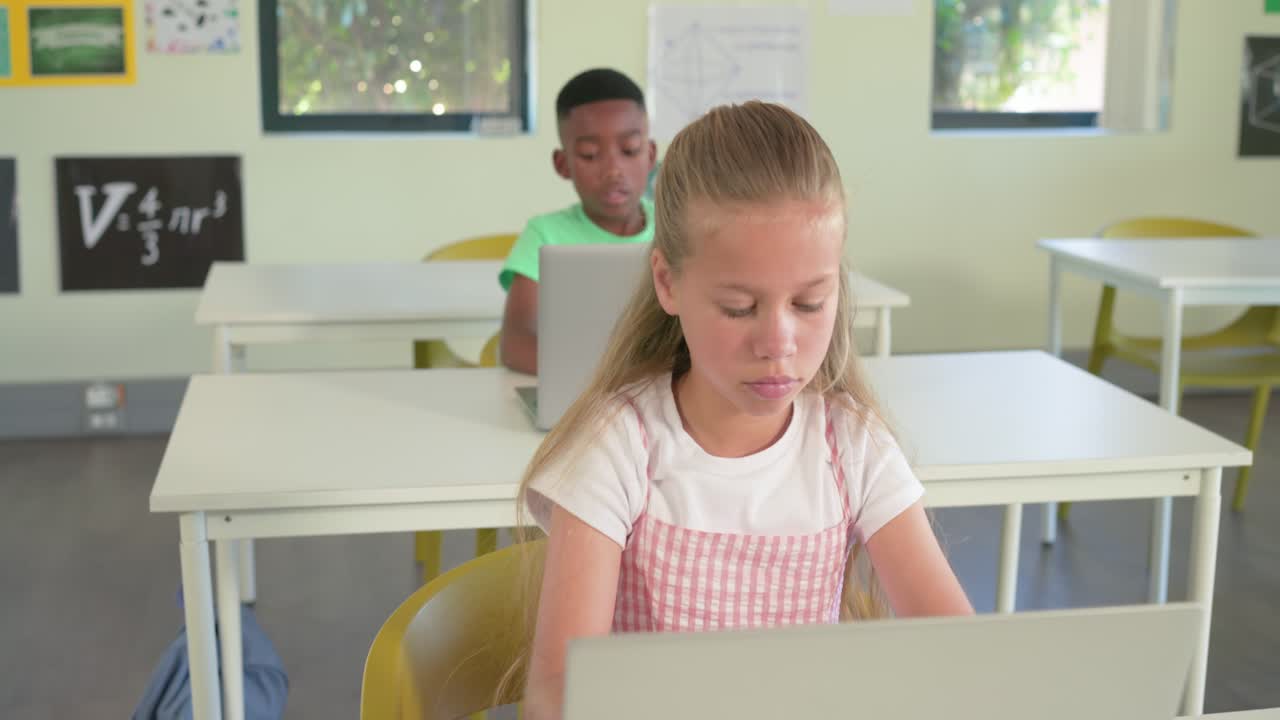 Bambini diversi in classe che digitano sui portatili mentre la camera restringe il disegno della ragazza che si ferma, pensando