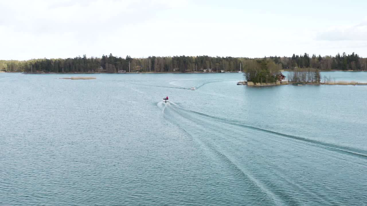 A drone follows a boat from on high catching it as it turns in the water and ends while lowering into the middle between the wave lines of the wake