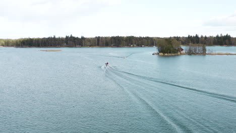 a drone follows a boat from on high catching it as it turns in the water and ends while lowering into the middle between the wave lines of the wake