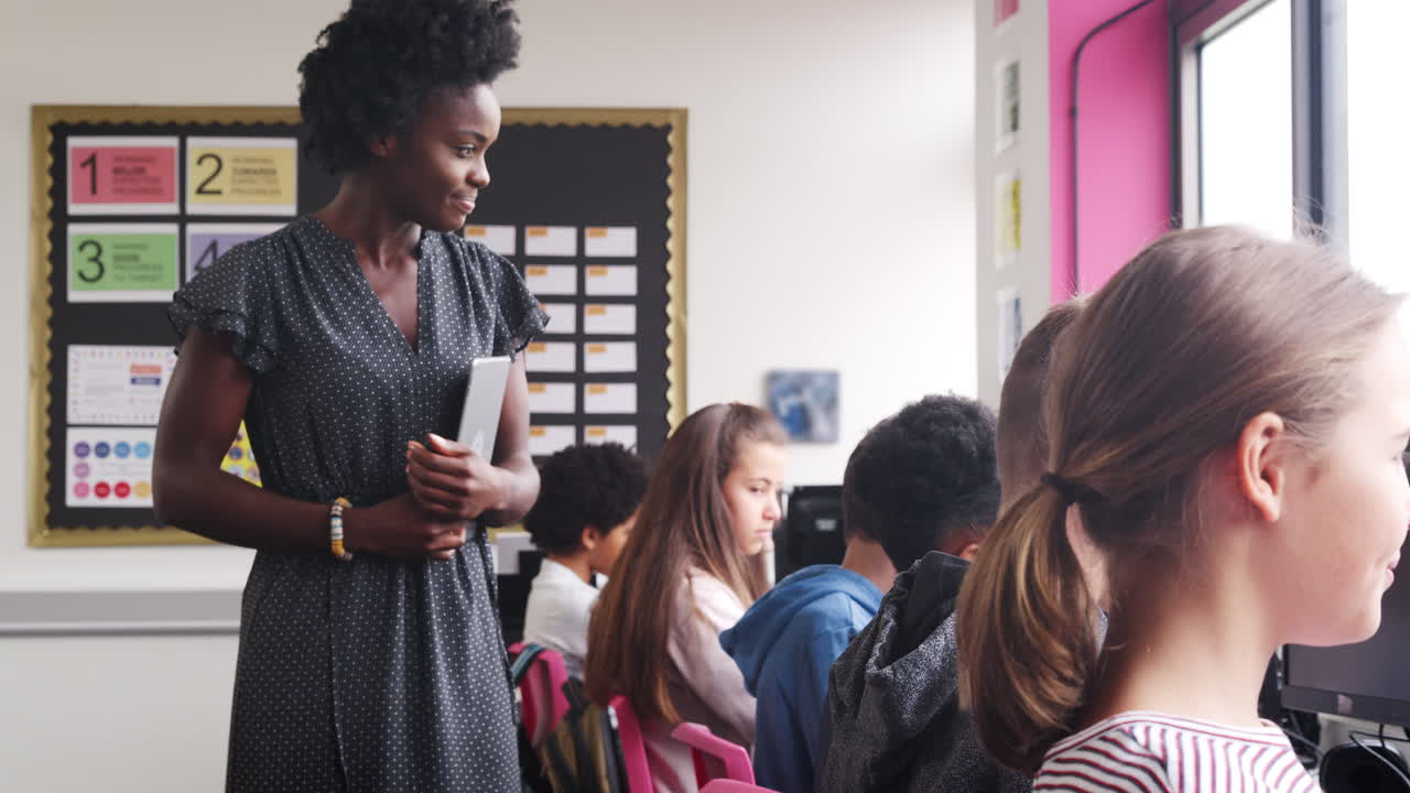 Insegnante femminile che supervisiona la linea di studenti delle scuole superiori che lavorano su schermi in classe di computer