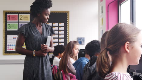 maestra supervisando la línea de estudiantes de secundaria que trabajan en pantallas en la clase de computadora