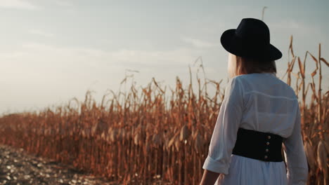 farmer in a dress and hat walks in a field of ripe corn