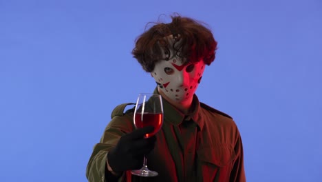 person in jason voorhees mask holding a glass of red liquid