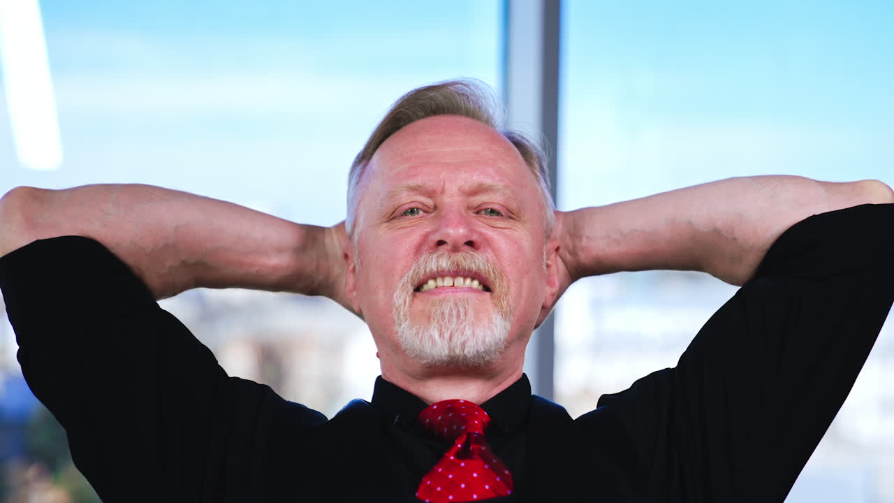 Happy relaxed man sits holding his hands behind his head. Close up portrait of a senior male.