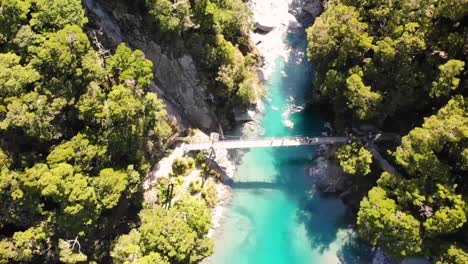 Drone-Volando-Sobre-El-Puente-Giratorio-Sobre-El-Agua-Prístina-En-La-Pista-De-Piscinas-Azules,-Costa-Oeste,-Nueva-Zelanda-Con-Bosques-Nativos-De-Hayas---Toma-Aérea-De-Arriba-Hacia-Abajo