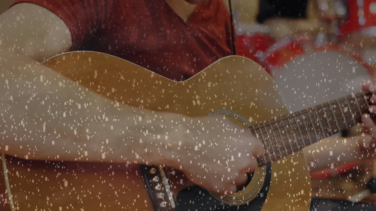 Male guitarist strumming acoustic guitar in recording studio, featuring snow overlay and drum icon