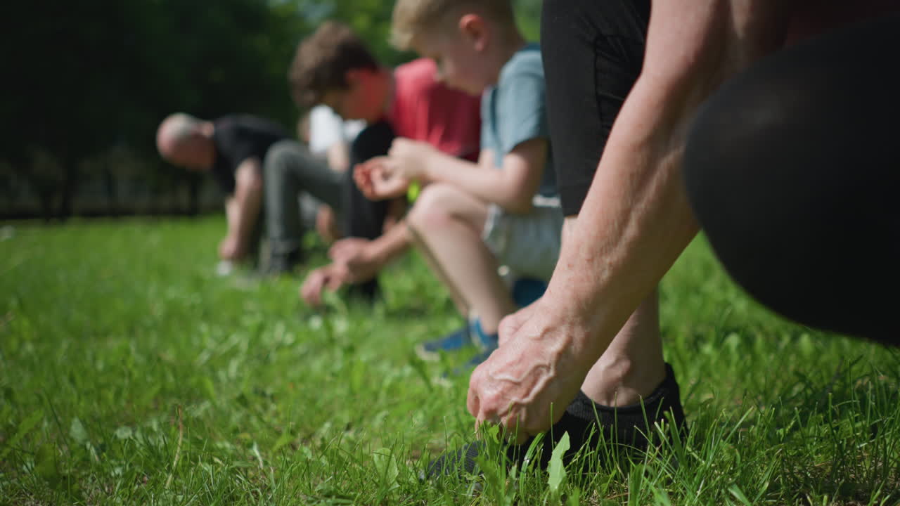 잔디에서 신발을 는 누군가의 가까운 모습. 배경에는 무을 숙고 있는 흐릿한 인물들이 보인다. 어떤 사람들은 신발를 고 다른 사람들은 다른 일을 하고 있다.