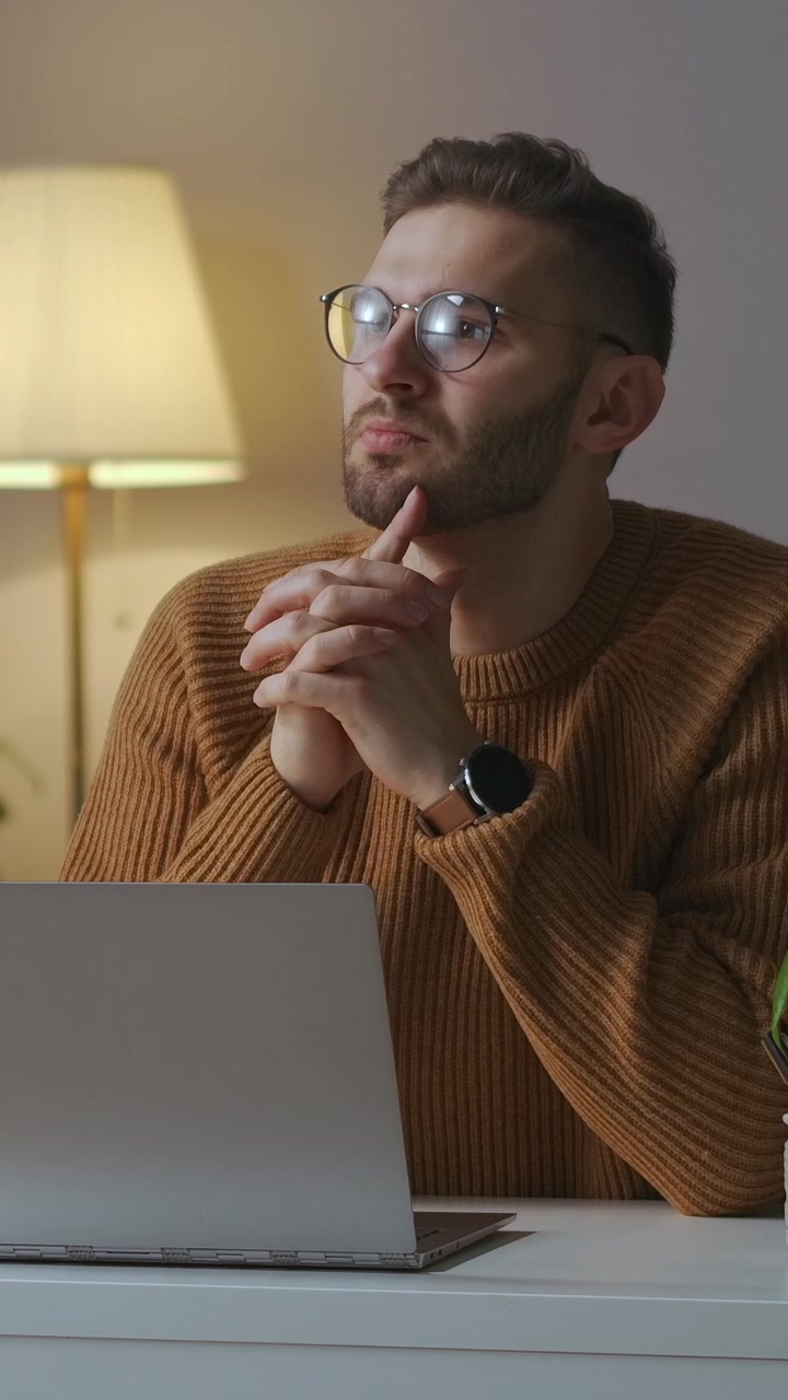 Uomo pensieroso con gli occhiali che lavora al laptop a casa