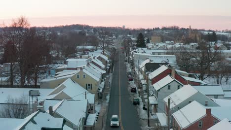 Aerial-of-cars-with-headlights-at-sunset-pass-along-quiet-street-through-town