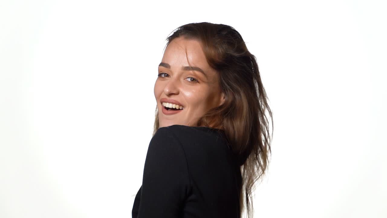 A passionate woman with brown hair tilts her hair back on a white background in the studio. Close-up.