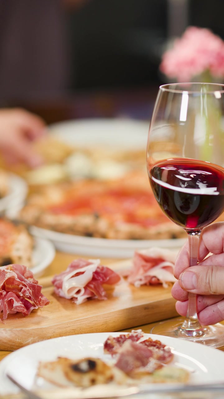 Primo piano di amici che condividono una cena italiana con pizza e vino sotto una calda illuminazione da ristorante.