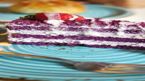 una rebanada de pastel púrpura con crema batida y una fresa