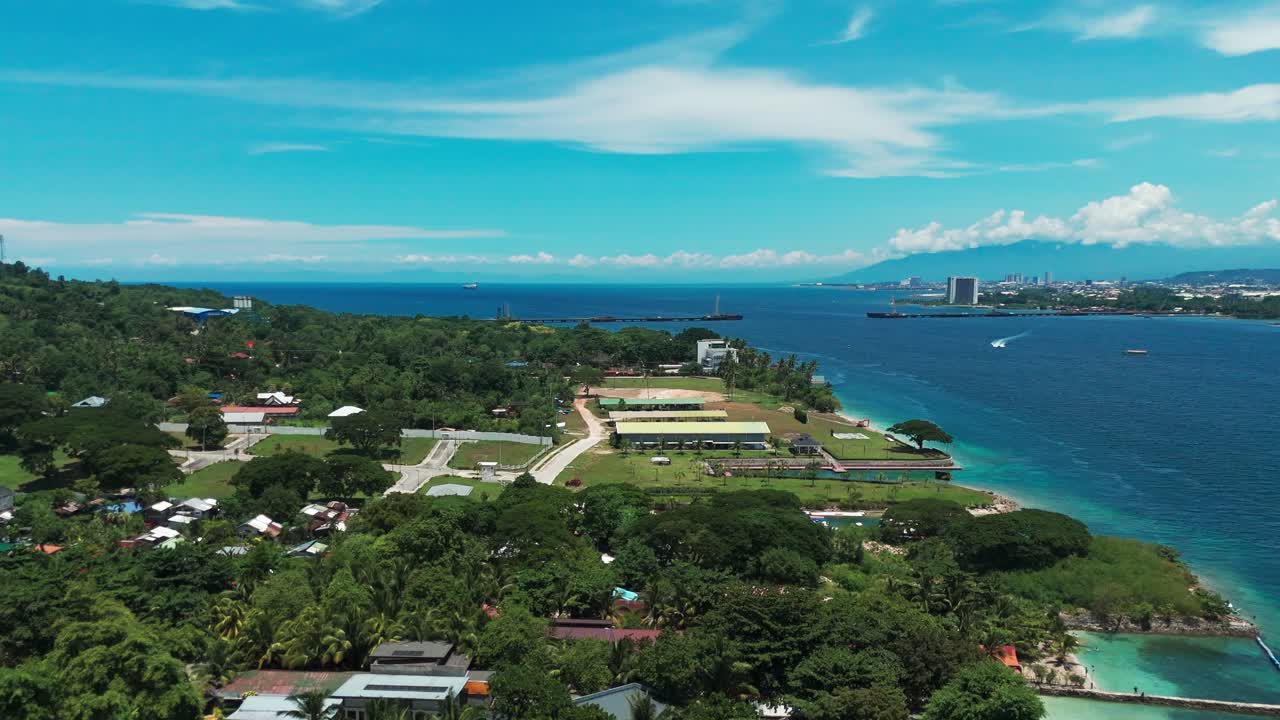 Drone aerial of a tropical coastal area with lush greenery, village houses, modern buildings, and city skyline by the sea. Perfect for travel, real estate, and urban development projects