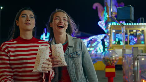 happy girls walking funfair festival on holiday. funny friends holding snacks