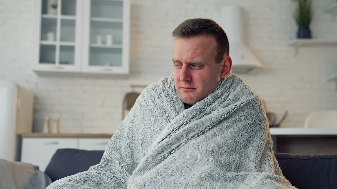 Sick man covered with warm blanket. Young man has a terrible headache and feeling ill at home. Infected man with virus. Coronavirus concept.