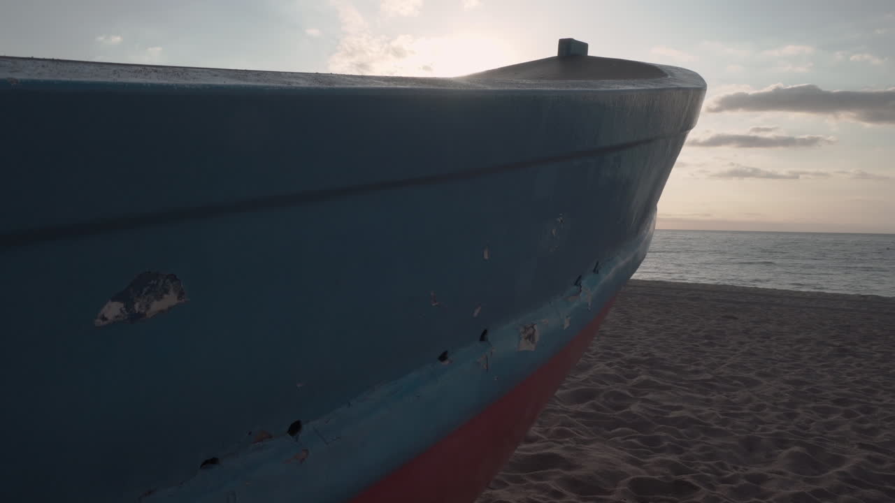 revelación de un clip de 4k de un pequeño bote de pescador clásico en la arena de una playa del mar mediterráneo al amanecer que muestra un estallido de sol y un cielo suave y nubes