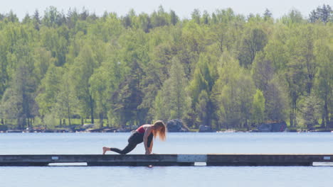Female yogi on wooden floating dock on lake doing yoga sequence, wide side view