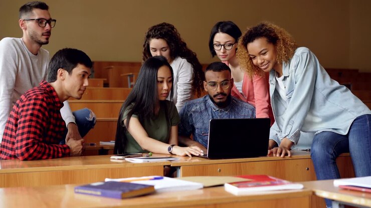 Un gruppo di studenti usa il laptop seduto in classe e conversa, i giovani lavorano a un progetto. Concetto di stile di vita moderno, istruzione universitaria e tecnologia.