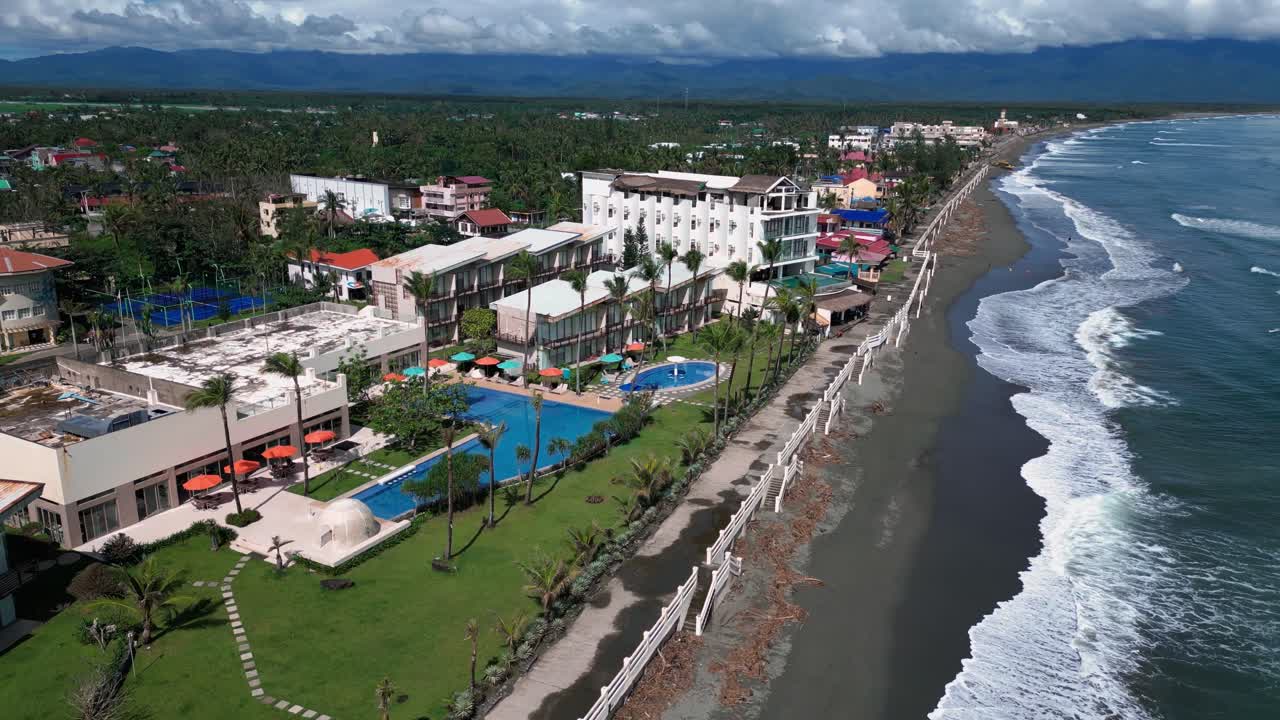 A broad drone shot reveals a stunning resort located along the coast, where the tranquil ocean waves softly kiss the sandy shore.