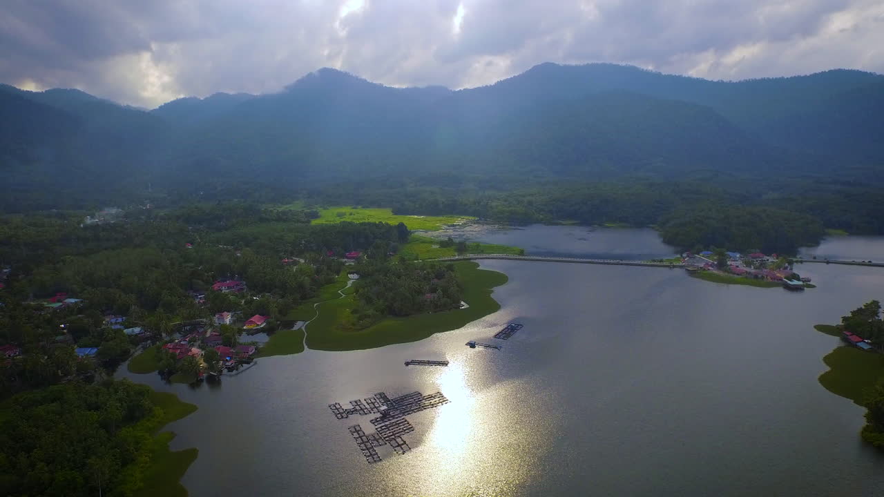 toma aérea del lago raban con montaña, piscifactoría y bosque durante la hermosa puesta de sol con dios ray, malasia