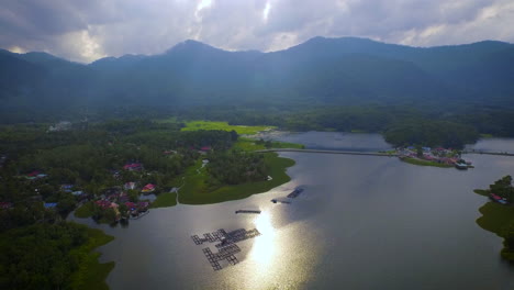 Toma-Aérea-Del-Lago-Raban-Con-Montaña,-Piscifactoría-Y-Bosque-Durante-La-Hermosa-Puesta-De-Sol-Con-Dios-Ray,-Malasia