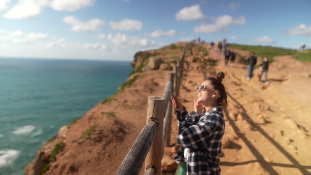 mujer tomando una foto en un acantilado con vistas al océano