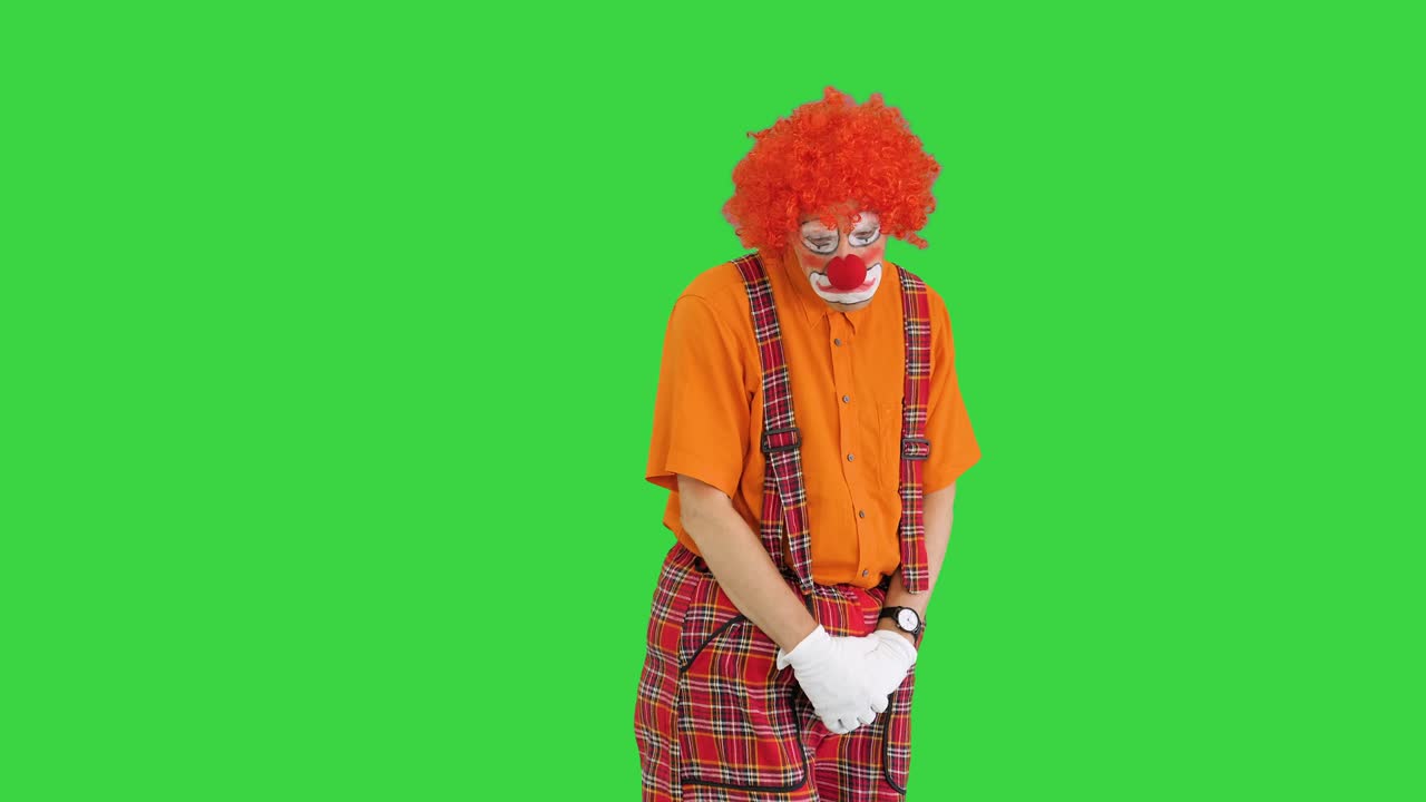 payaso infeliz de pie y estar nervioso en una pantalla verde, clave de croma