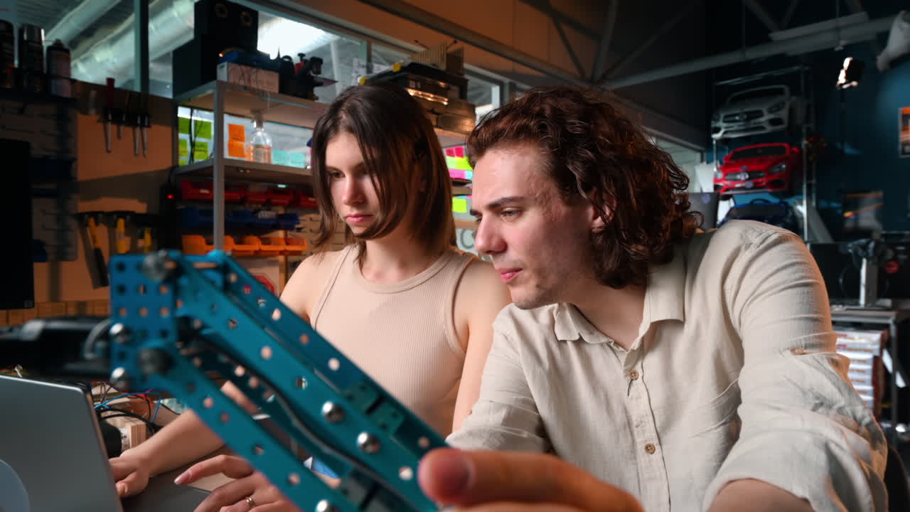 Young man and woman doing experiments in robotics in a laboratory using a computer. Robot and tools on the table