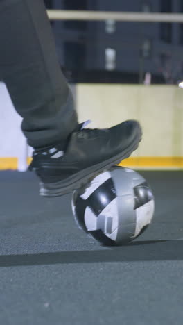 back view of soccer player kicking soccer ball toward goalpost, wearing athletic shoes and sweatpants, with goalpost in focus, illuminated under bright night lighting