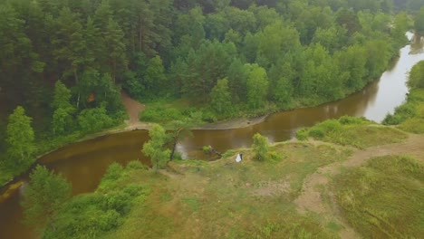 newlywed couple on bank of river at green forest aerial view