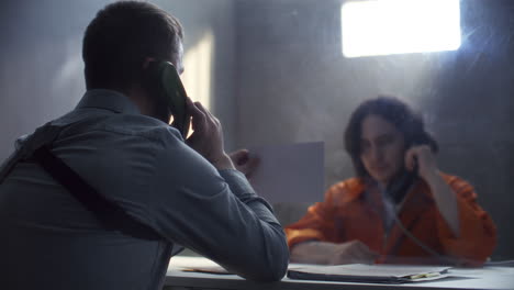 officer conducting interrogation through glass partition in prison room