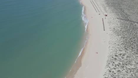 Vista-Aérea-De-Una-Playa-De-Arena-Amarilla-Con-Sombrillas-A-Lo-Largo-De-La-Orilla