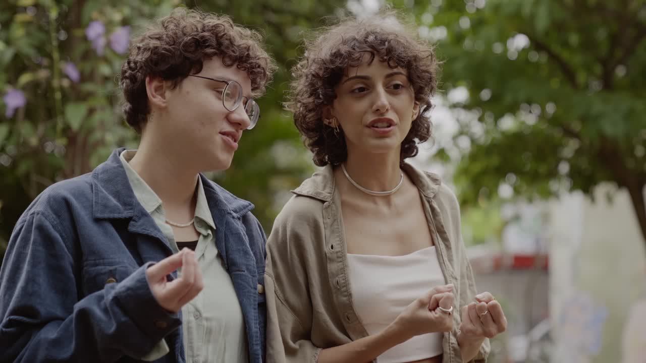 Two young women with curly hair having a conversation outdoors