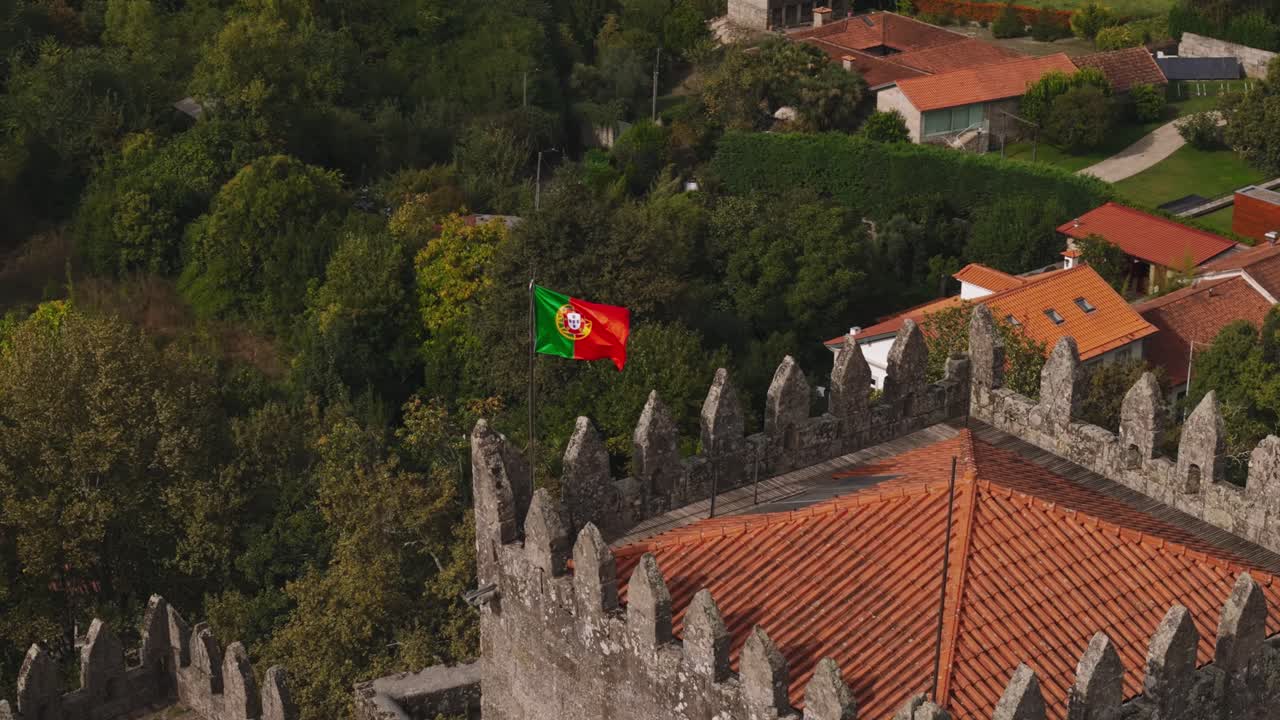 historic Guimarães Castle with Portuguese flag flying above medieval stone walls in Portugal - aerial