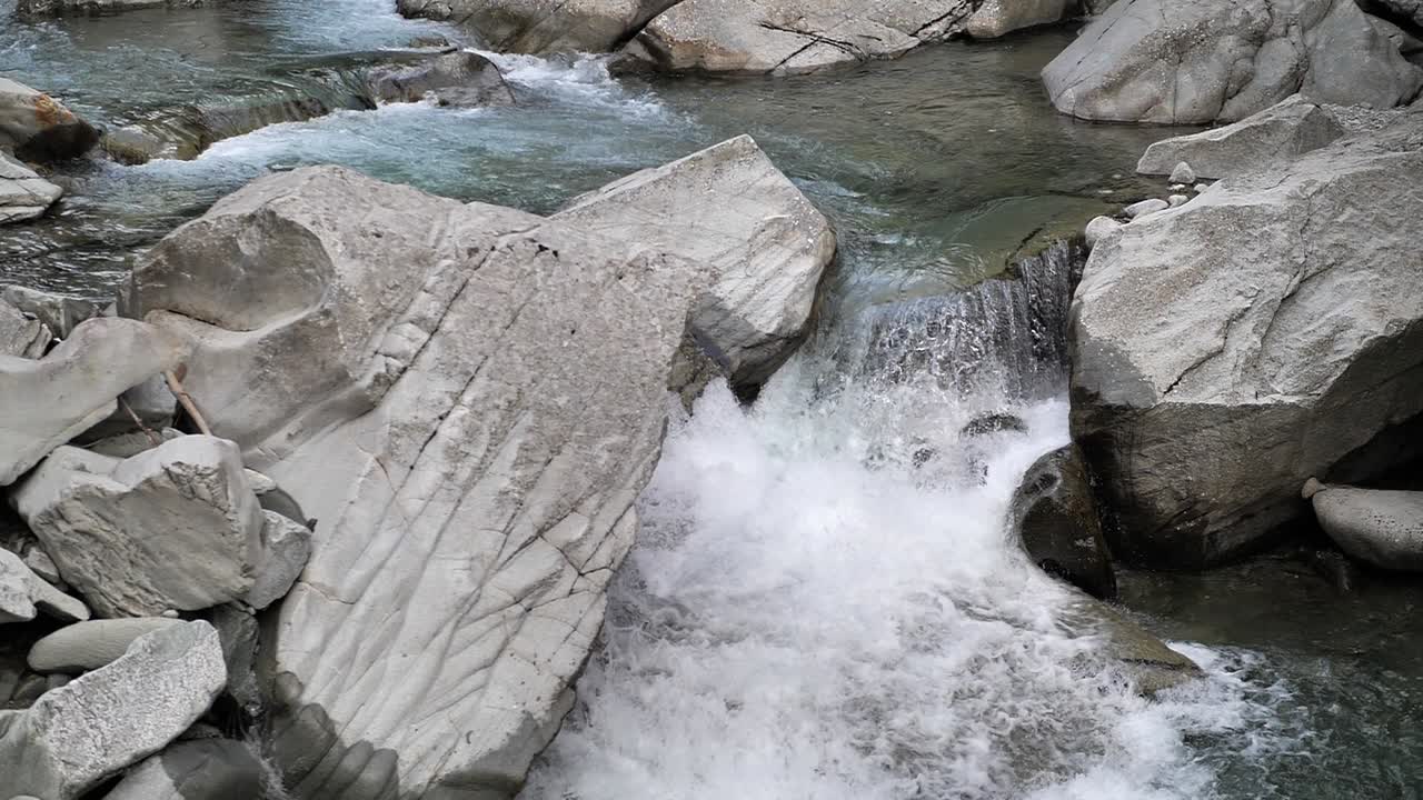 Clear blue water streaming true the rocks and falling down on a small waterfall in Lauterbrunnen Switserland. Medium slowmo shot.
