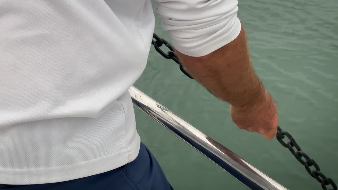 marinero con una camisa blanca agarra y tira de una cadena de ancla de un bote pequeño